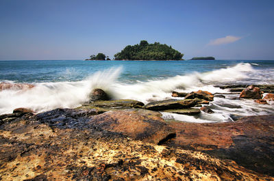Waves splashing on rocks at shore against sky