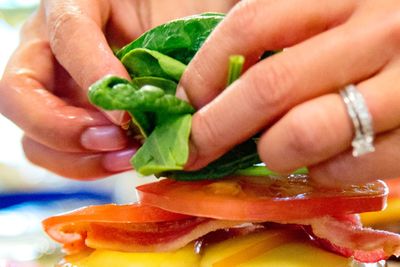 Cropped hand of woman preparing bacon cheeseburger