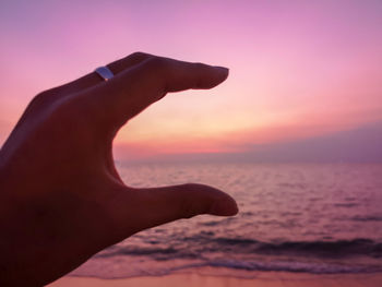 Low angle view of human hand on beach during sunset