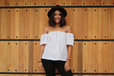 Portrait of smiling woman standing against wooden wall