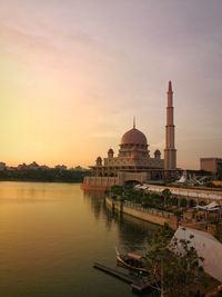 Mosque by river against sky during sunset