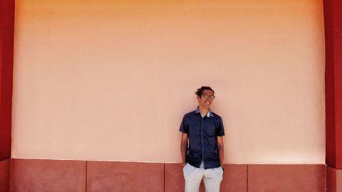 Young man looking away while standing by wall