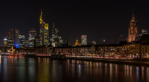 Illuminated buildings by river against sky in city at night