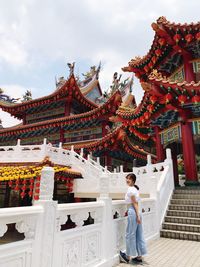 Full length of woman standing by railing in temple against sky