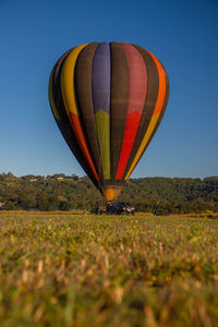 Hot air balloons on field against clear blue sky