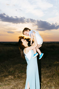 Couple standing on field against sky during sunset