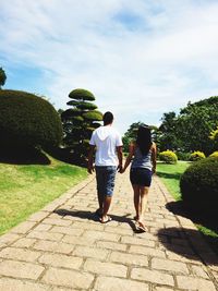 Rear view of couple walking on footpath in park against sky