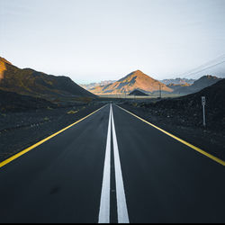 Empty road leading towards mountains against sky