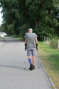 A man with a broken leg is walking down the street, on his left leg he has  special boot for walking