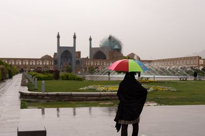 Rear view of woman with umbrella against sky during rainy season
