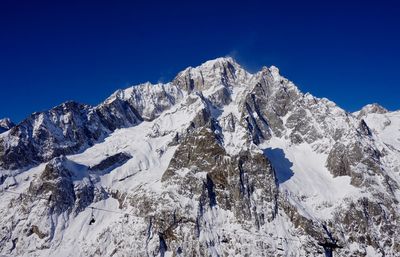 Low angle view of snowcapped mountains against clear blue sky