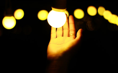 Close-up of hand by illuminated light bulb