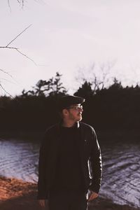 Man looking away while standing by lake against sky