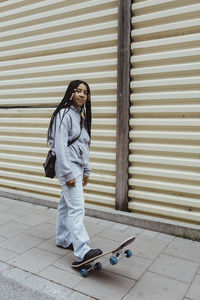 Teenage girl with skateboard on footpath by metal wall