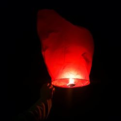 Close-up of hand holding illuminated lantern over black background