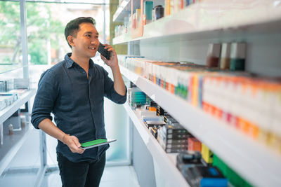 Side view of young man using mobile phone in supermarket