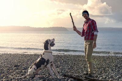 Portrait of smiling mature man with dog at beach against cloudy sky