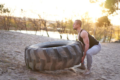 Side view of young man picking up tire on land