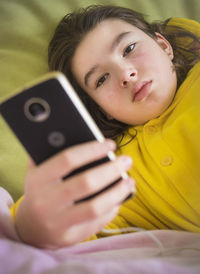 Girl using mobile phone while lying on bed at home