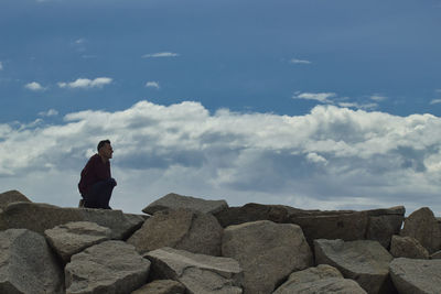 Man on top of a stone breakwater looking at the horizon with blue sky background