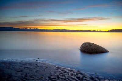 Rock in lake against sky during sunset