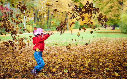 Girl throwing leaves at park during autumn