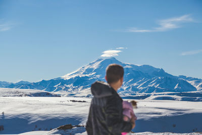 Rear view of man standing on snowcapped mountains against sky
