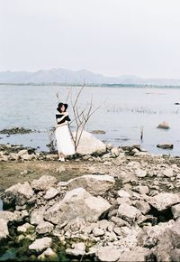 Rear view of person on rock at beach against sky