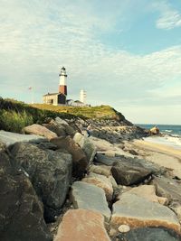 Lighthouse on rocks by sea against sky