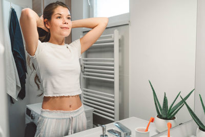 Portrait of young woman standing against wall at home