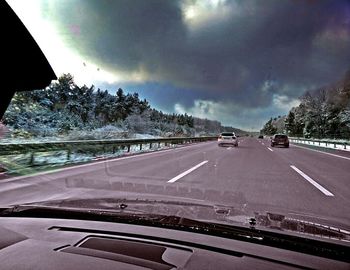 Cars on road against cloudy sky