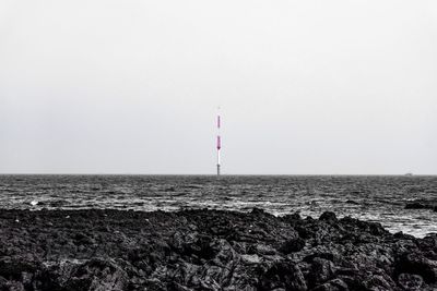 Lighthouse by sea against clear sky