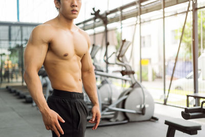 Midsection of shirtless male athlete standing in gym