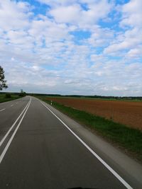 Empty road amidst field against sky