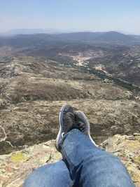 Low section of man sitting on rocky mountain against landscape