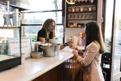 Young businesswoman paying through credit card at counter in coffee shop during covid-19