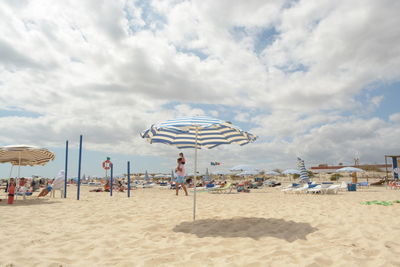 People enjoying at beach against cloudy sky