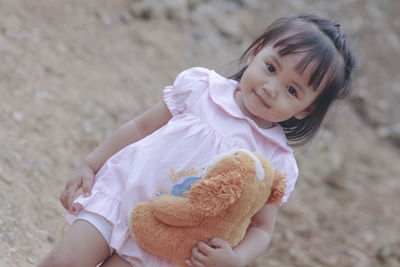Portrait of cute smiling baby girl holding stuffed toy outdoors