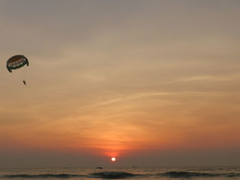 Hot air balloon flying over sea against sky during sunset