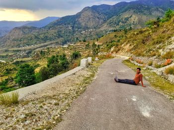 Side view of man sitting on road against mountains