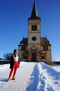 Full length of woman standing on snow covered landscape against church