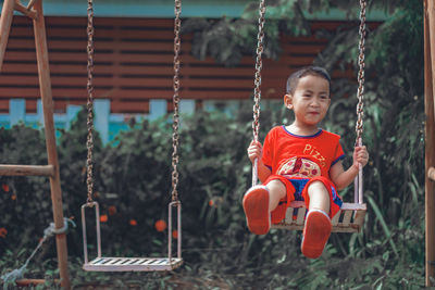 Cute boy sitting on swing at playground