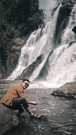 Full length of man splashing water by waterfall