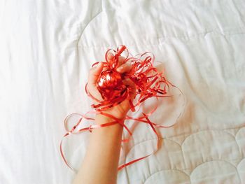 Cropped image of hand holding red ribbon on bed