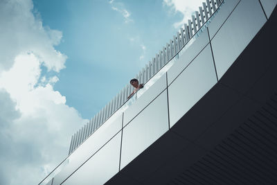 Low angle view of man looking away while standing in balcony against sky