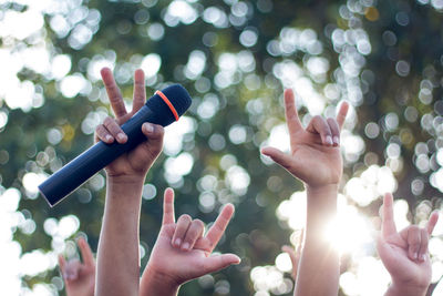 Cropped hand of person holding microphone against trees
