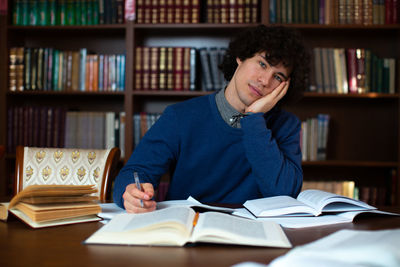 Portrait of thoughtful young man sitting with books on table