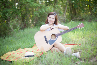 Young woman with guitar on grassy field at park