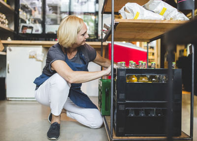 Full length of female employee arranging crates on rack in deli