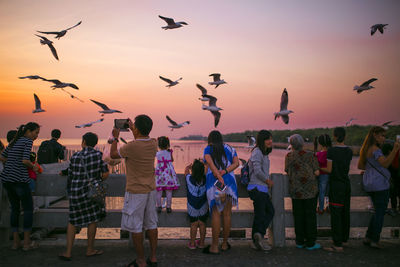 People standing by railing against sky during sunset